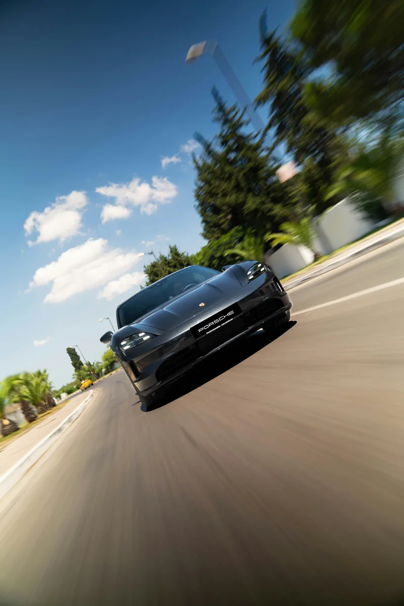 Porsche Taycan gris en movimiento por una carretera con palmeras